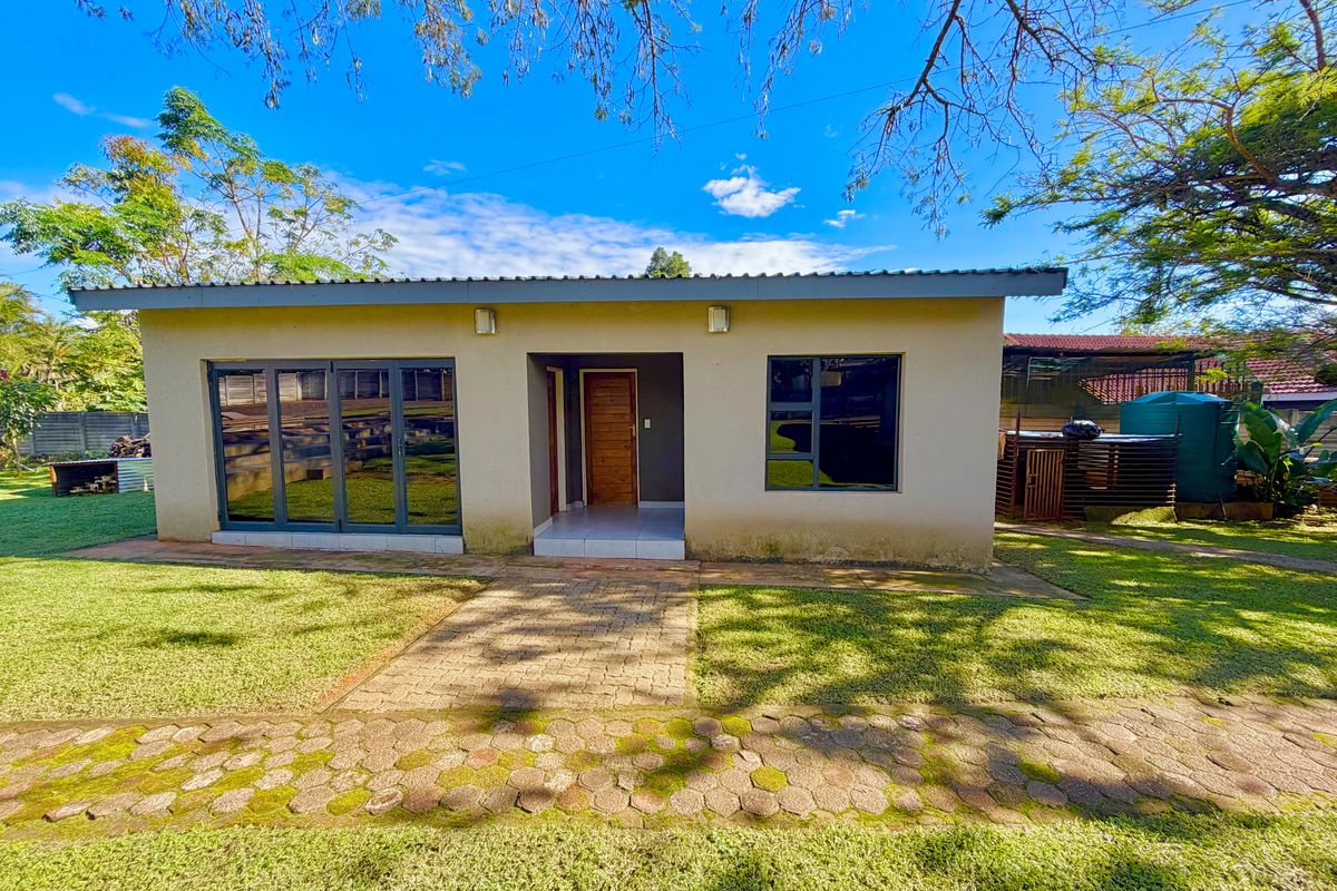 Rear view of a single-story home featuring aluminium sliding doors, a paved walkway, and a well-maintained garden area.
