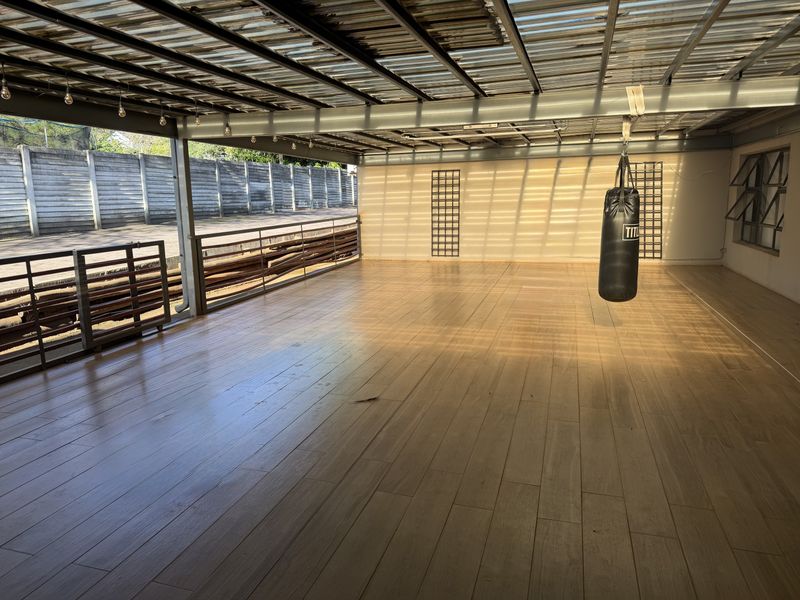 A spacious covered patio featuring timber-look tile flooring, a metal roof structure, and a metal balustrade, offering a versatile outdoor entertainment area.