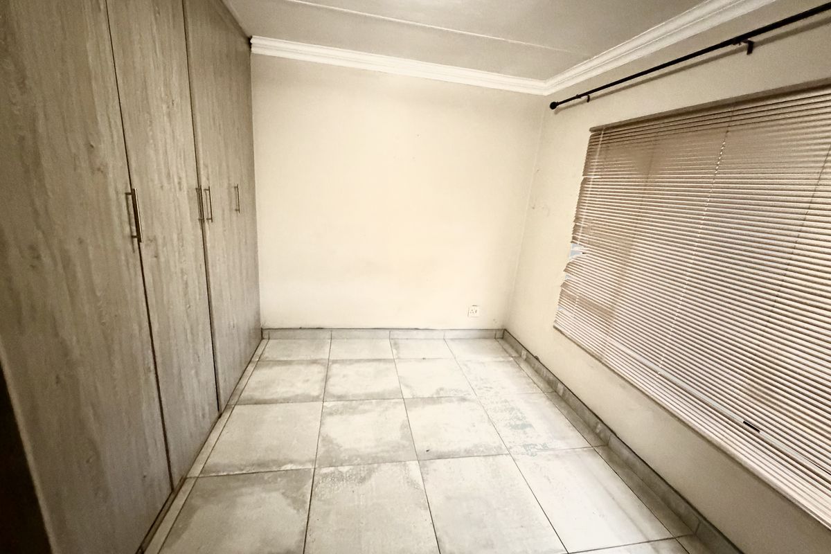 An empty bedroom featuring tiled flooring, built-in cupboards, and venetian blinds, offering a blank canvas for personalization.