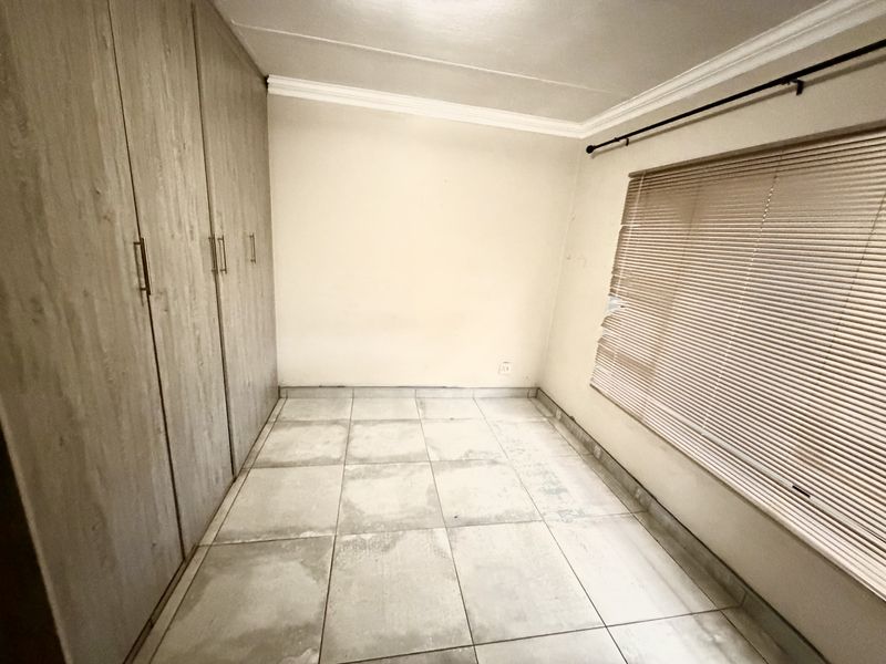 An empty bedroom featuring tiled flooring, built-in cupboards, and venetian blinds, offering a blank canvas for personalization.