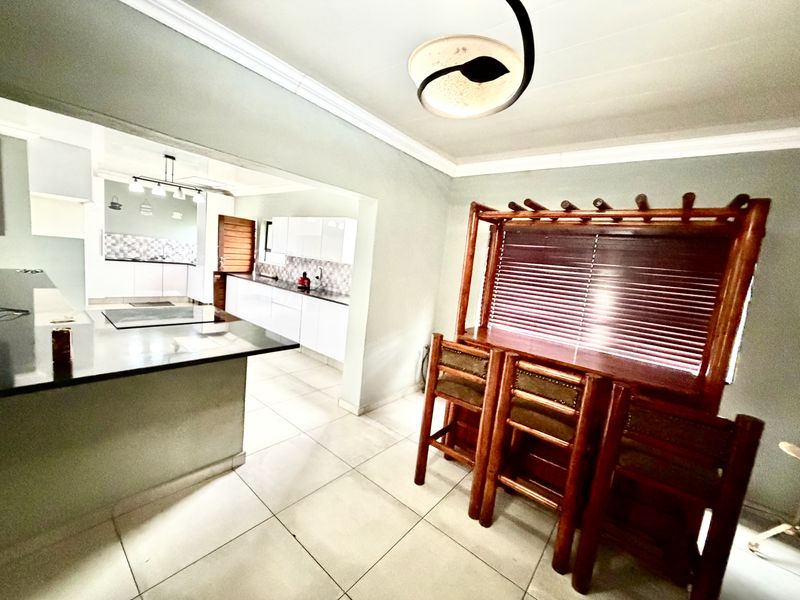 Open plan kitchen and dining area featuring modern white cabinetry, stone countertops, tiled flooring, and a built-in breakfast bar with integrated seating.