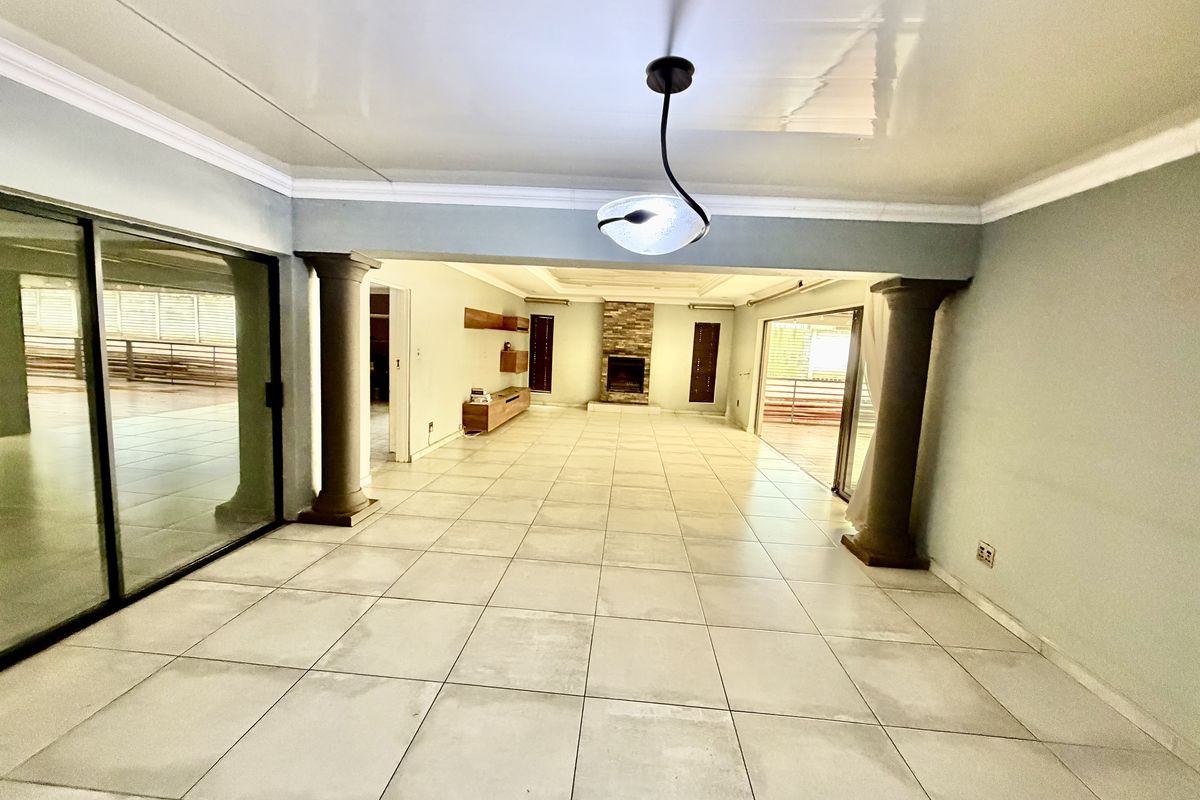 Spacious open-plan living area featuring large format floor tiles, a stone-clad fireplace, decorative columns, and sliding glass doors leading to outdoor spaces.