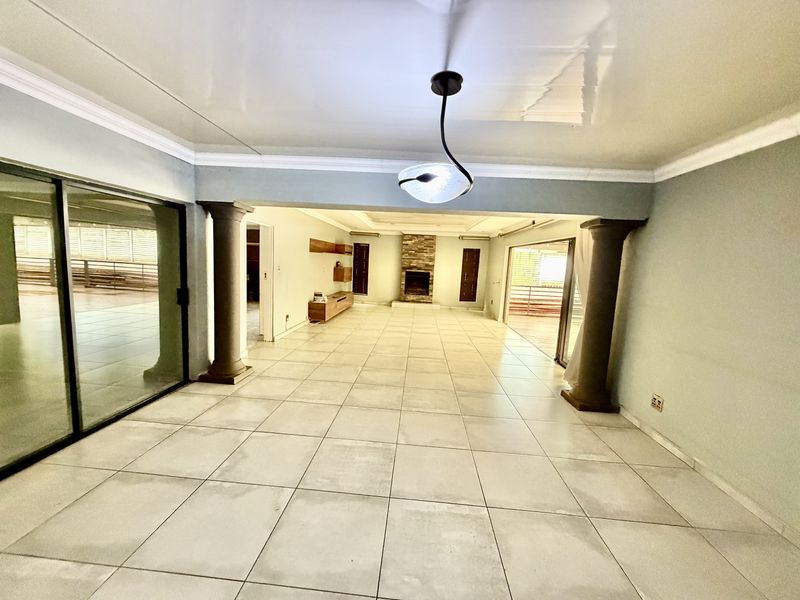 Spacious open-plan living area featuring large format floor tiles, a stone-clad fireplace, decorative columns, and sliding glass doors leading to outdoor spaces.