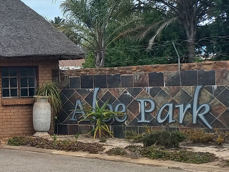 Entrance view of Aloe Park featuring a brick structure with a thatch roof and a stone-clad boundary wall with security fencing.