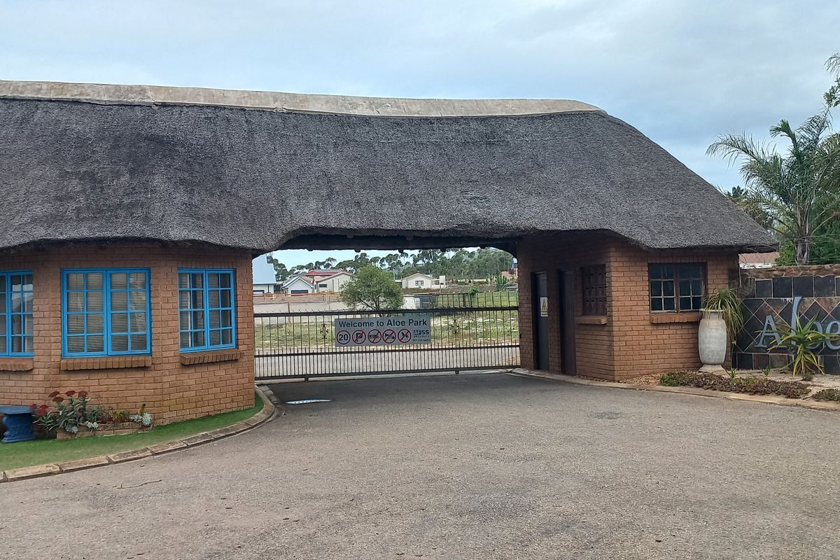 The entrance gate to Aloe Park, featuring a traditional thatched roof structure, brick masonry, and secure gated access.