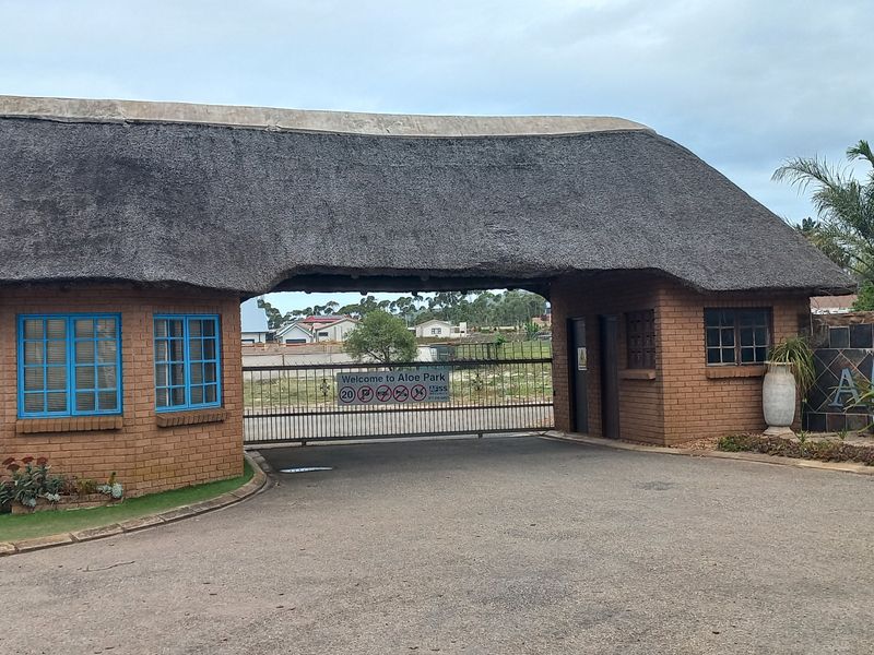 The entrance gate to Aloe Park, featuring a traditional thatched roof structure, brick masonry, and secure gated access.
