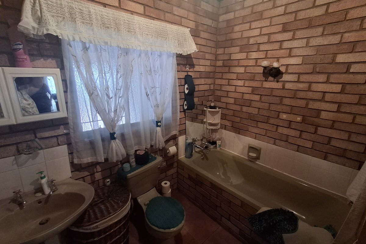 A dated bathroom featuring exposed brick walls, a built-in bathtub, a pedestal washbasin, and a toilet.