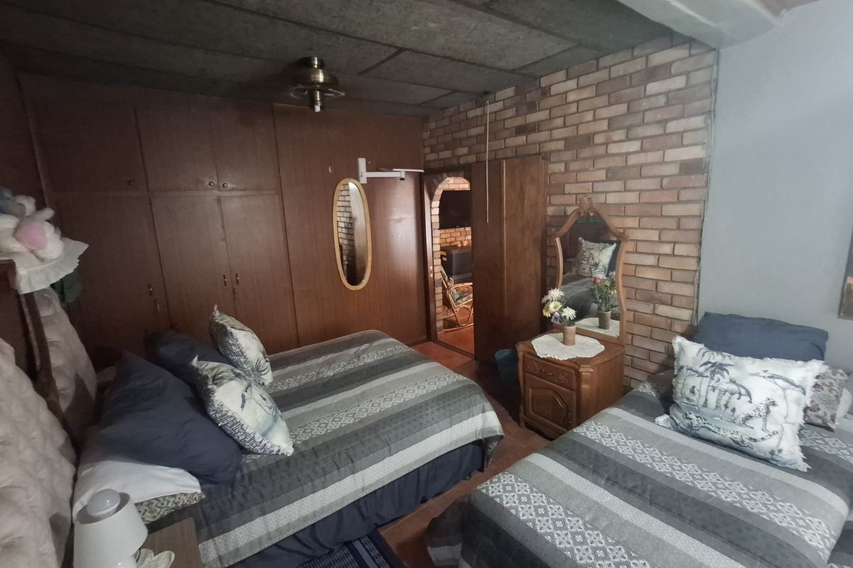 A bedroom featuring built-in wooden cupboards, an exposed brick feature wall, and a ceiling fan, with a doorway leading to an adjacent living space.