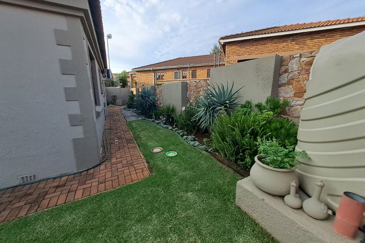 A well-maintained rear garden featuring a brick paved walkway, landscaped greenery, stone-accented boundary walls, and a functional water storage tank.