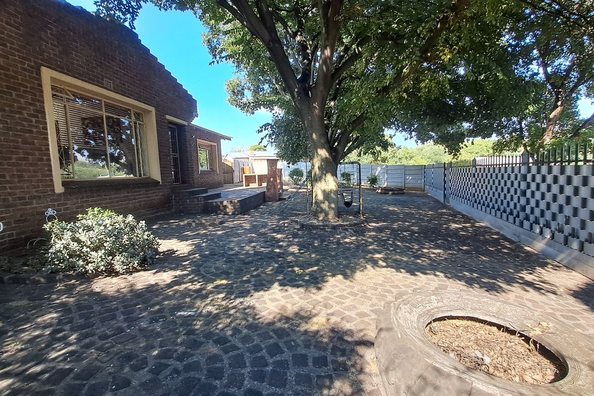 A spacious rear courtyard featuring brick exterior walls, paved flooring, and established trees, providing a private outdoor area for the property.