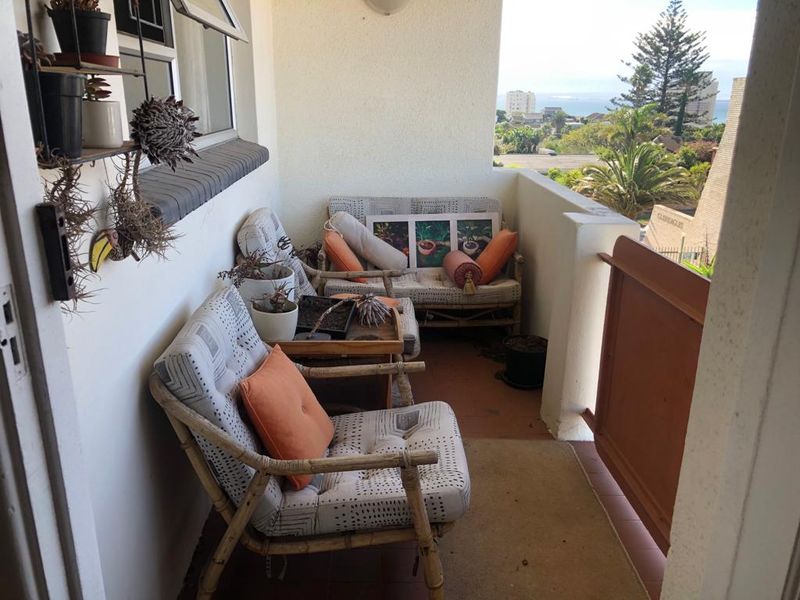 A covered balcony area featuring tiled flooring and a balustrade, offering an elevated view of the surrounding neighborhood and distant coastal landscape.