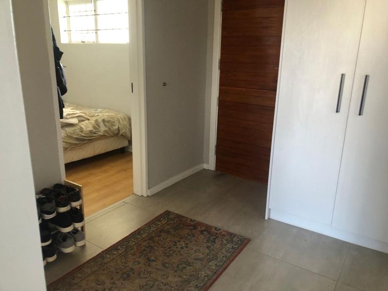 A functional hallway featuring tiled flooring, a built-in white cupboard, and a wooden door, providing access to an adjacent bedroom with laminate flooring.