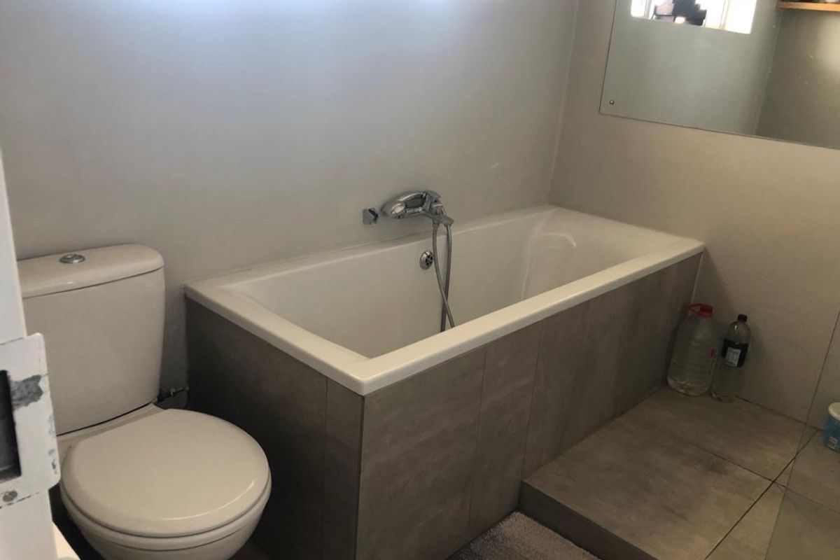A functional bathroom featuring a built-in bathtub with tiled surround, a standard toilet, and a large wall-mounted mirror.