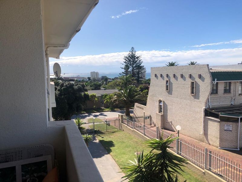 A view from an apartment balcony overlooking the surrounding neighborhood, garden area, and distant sea view.