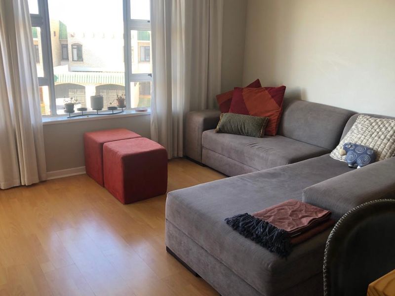 A bright living room featuring light-toned laminate flooring and a large window that provides natural light and a view of the exterior.