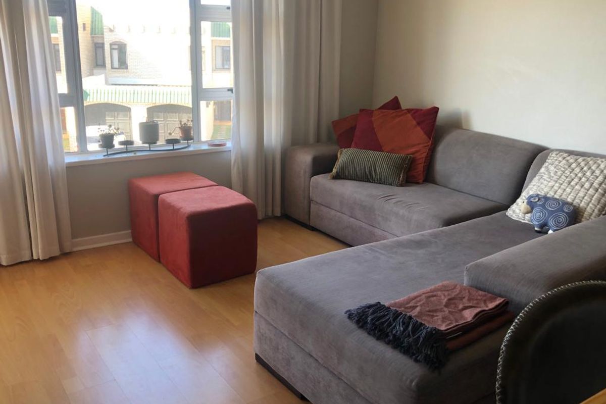 A bright living room featuring light-toned laminate flooring and a large window that provides natural light and a view of the exterior.