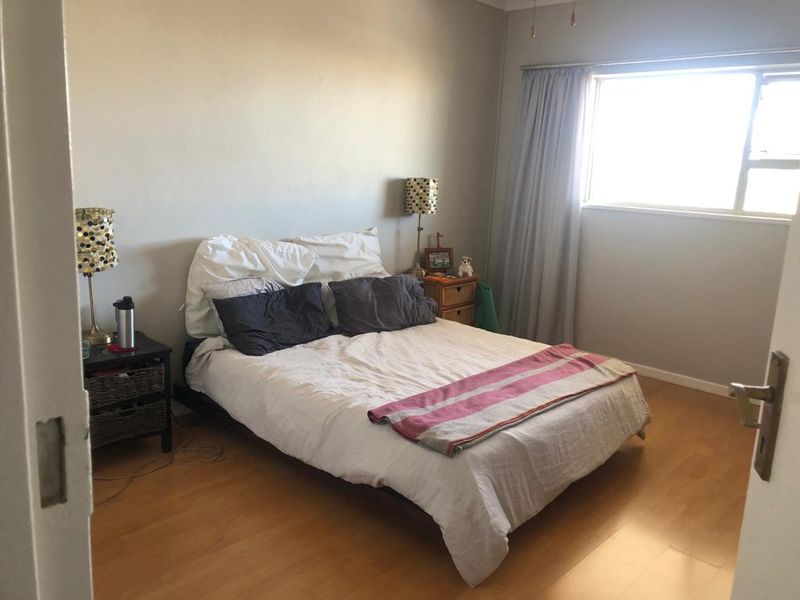 A functional bedroom featuring laminate flooring and a large window with curtain tracks, providing natural light and a neutral backdrop.