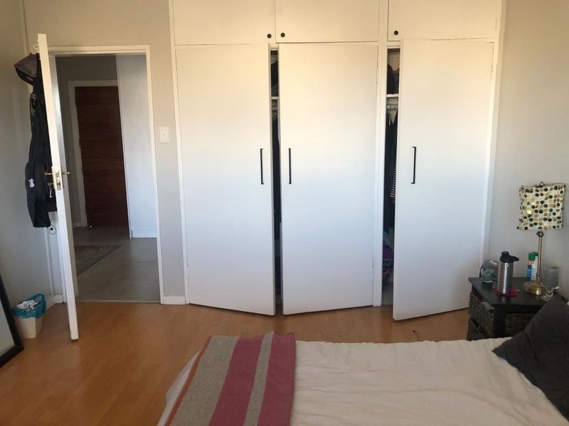 A bedroom featuring laminate flooring and white built-in cupboards with overhead storage, providing functional storage space.