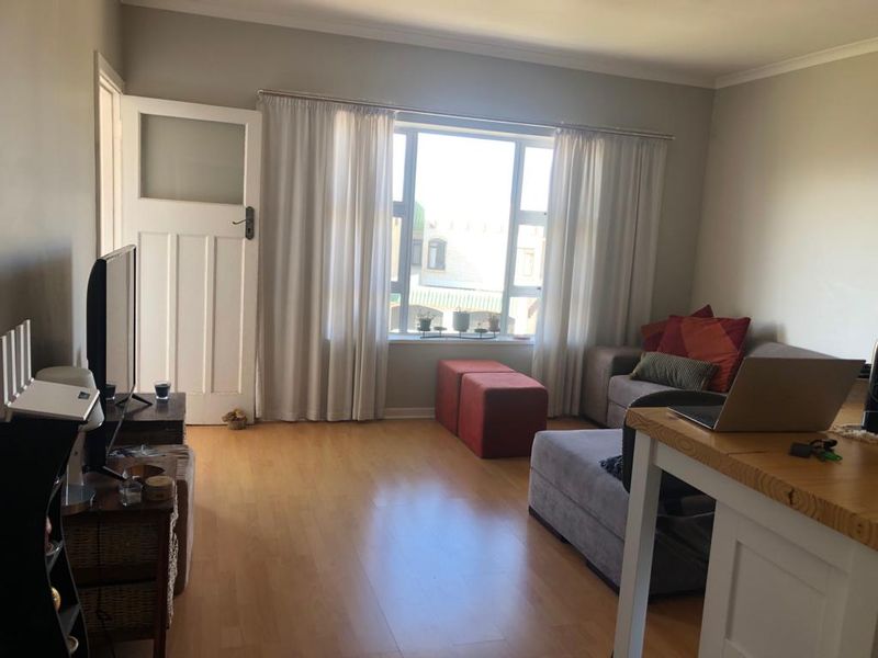 A comfortable living room featuring laminate flooring, a large window allowing natural light, and a classic panel door.