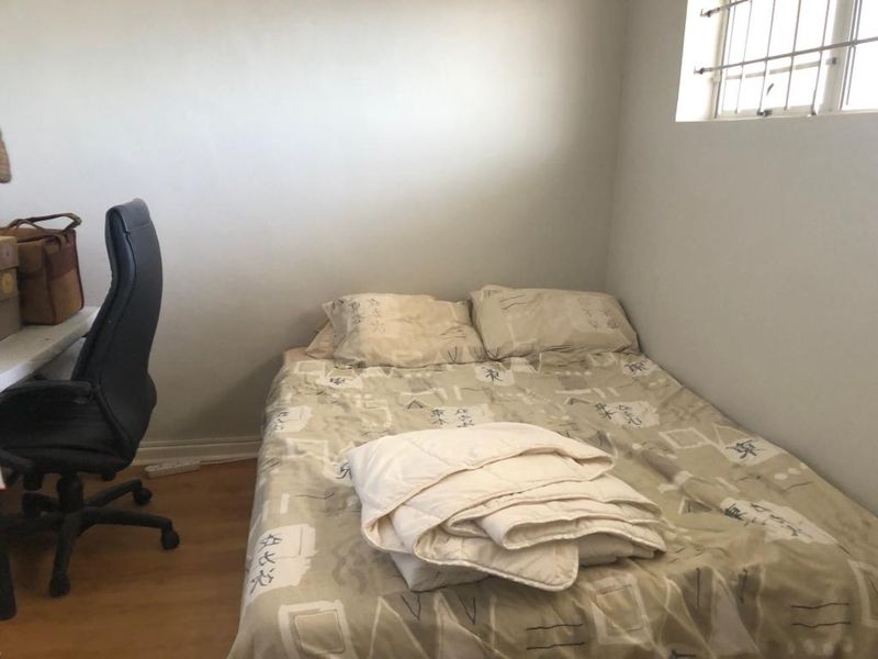 A compact bedroom featuring laminate flooring and a window fitted with security bars.