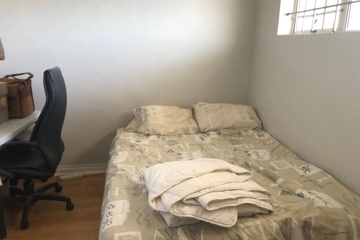 A compact bedroom featuring laminate flooring and a window fitted with security bars.