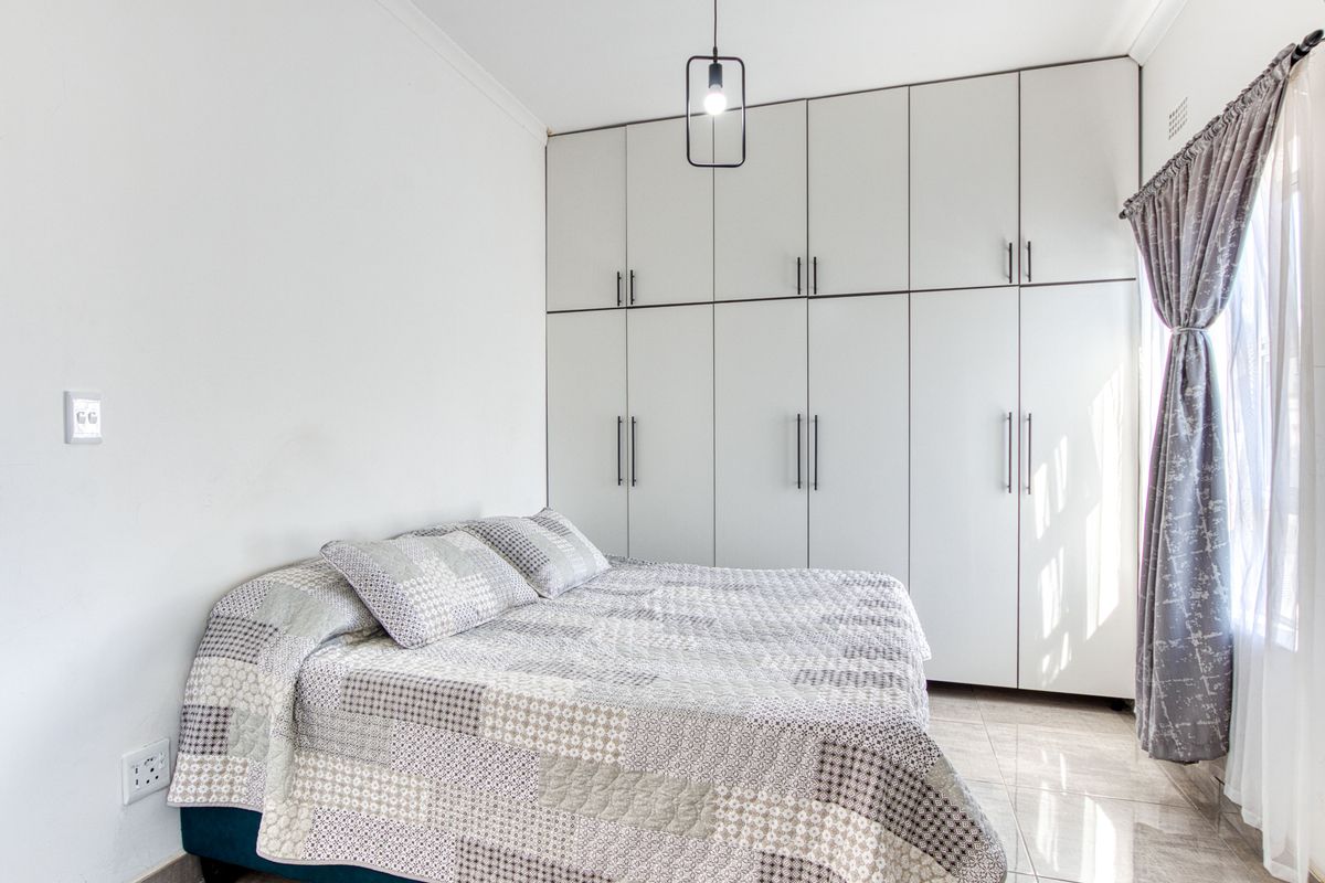 A bright bedroom featuring extensive floor-to-ceiling built-in cupboards, neutral tiled flooring, and a modern pendant light fixture.