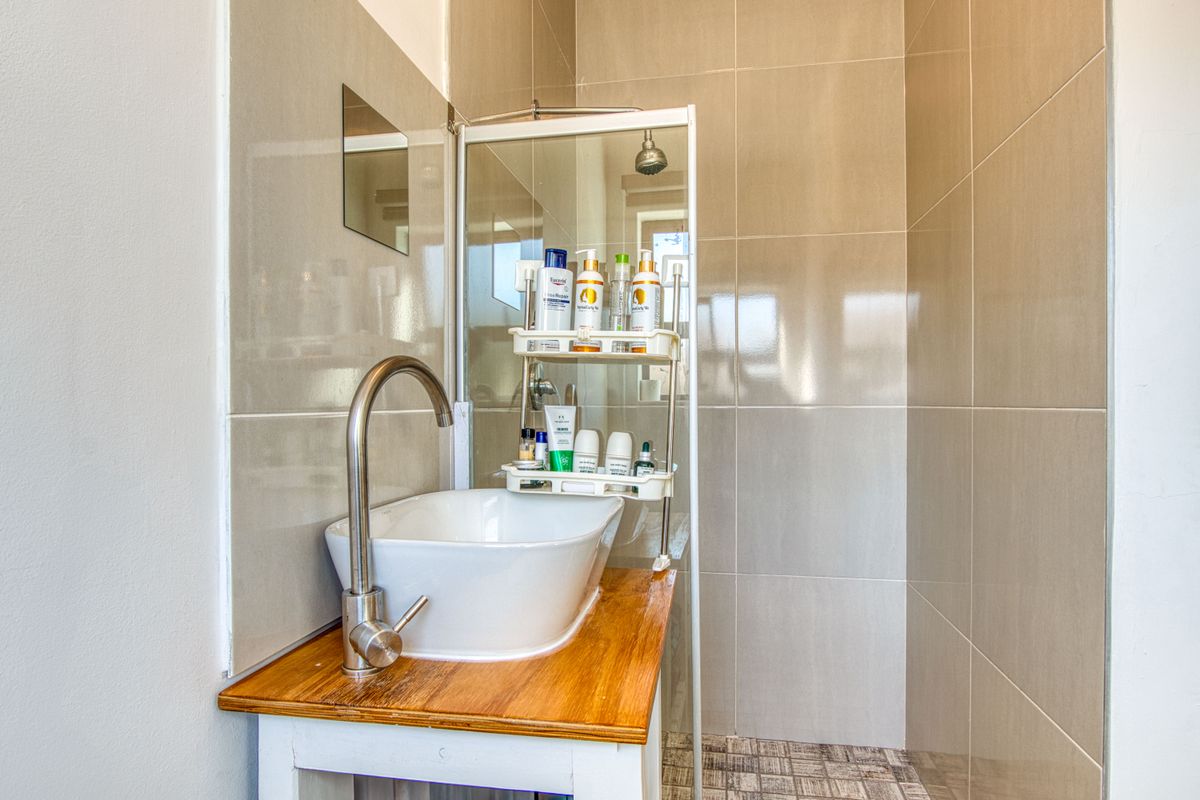 A compact bathroom featuring a modern vessel sink on a wooden vanity, a glass-enclosed shower, and neutral ceramic wall tiling.