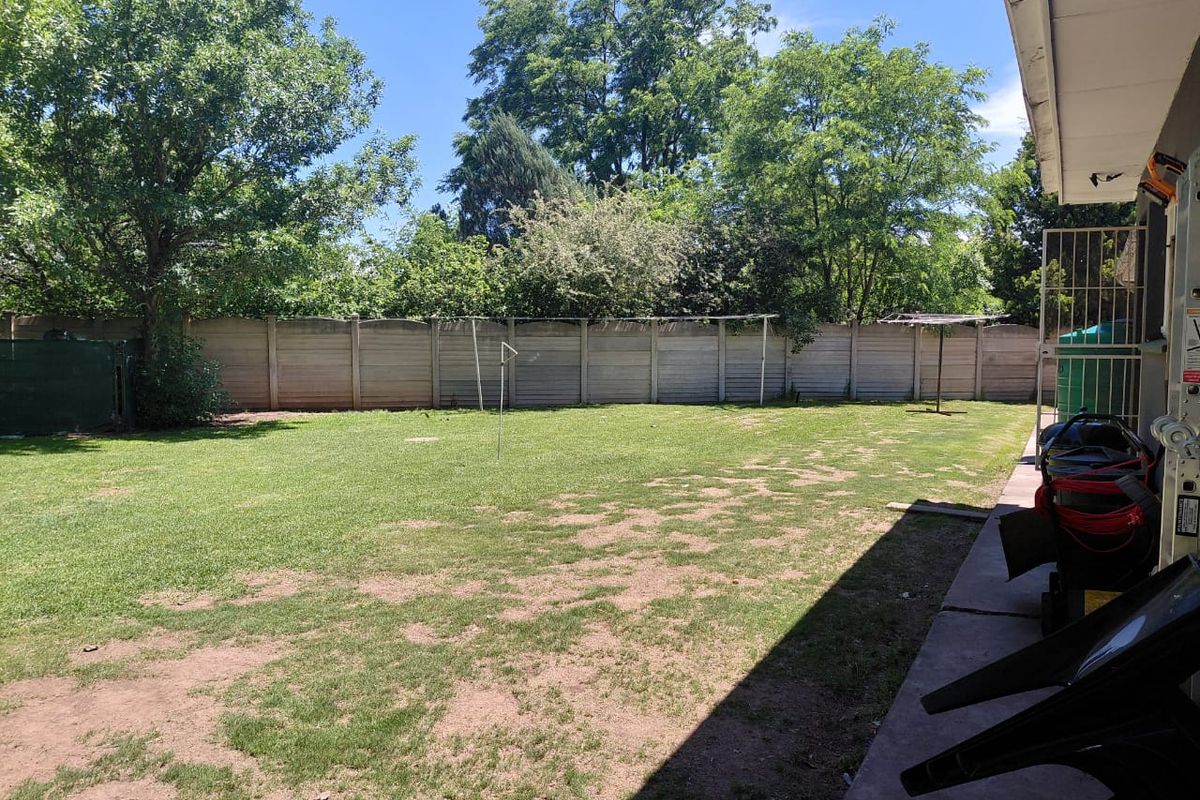 A spacious rear garden featuring a level lawn area, concrete patio, and a secure precast concrete boundary wall.