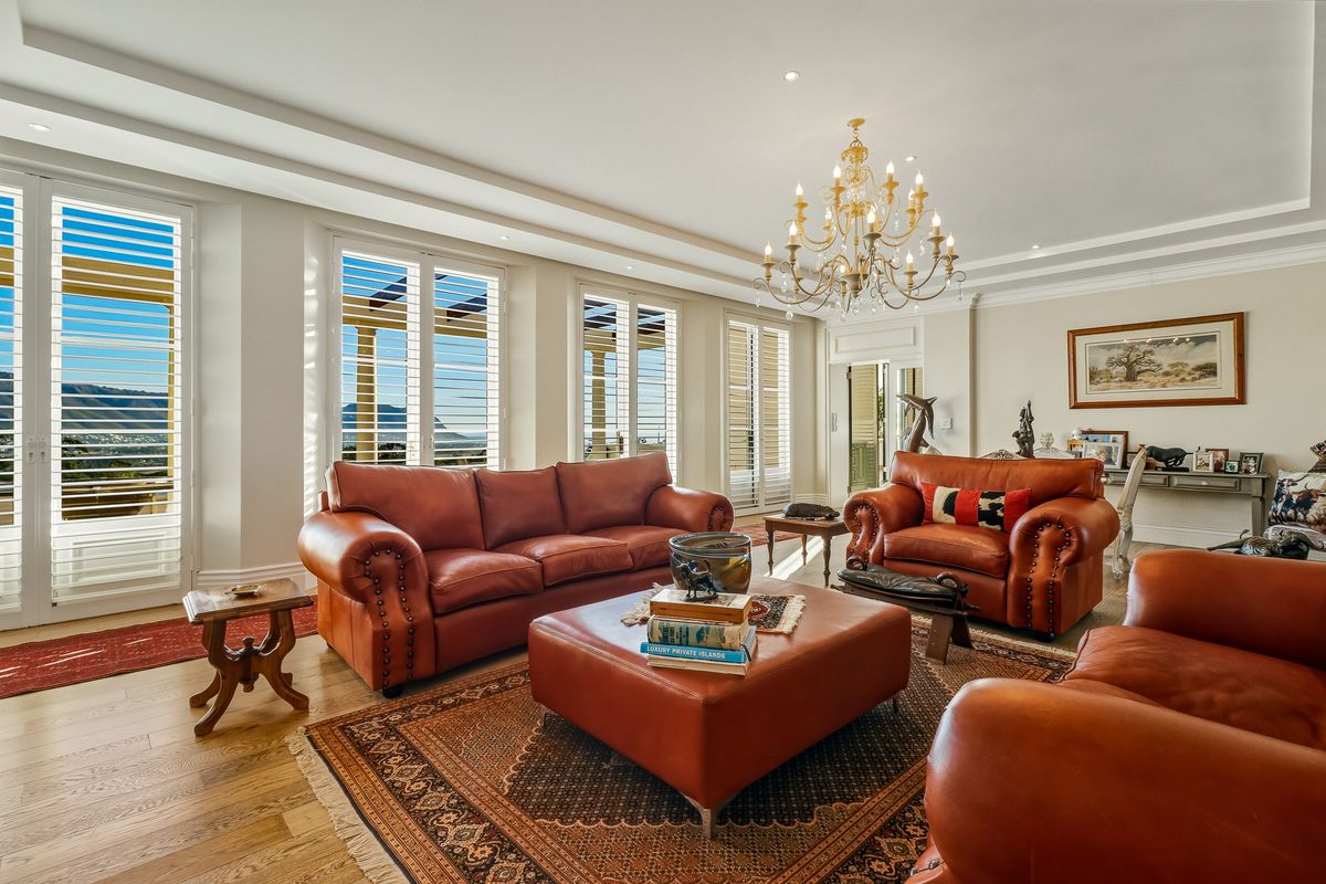 Spacious living room featuring hardwood flooring, elegant chandelier lighting, cove ceilings, and multiple sets of french doors with plantation shutters opening to the exterior.