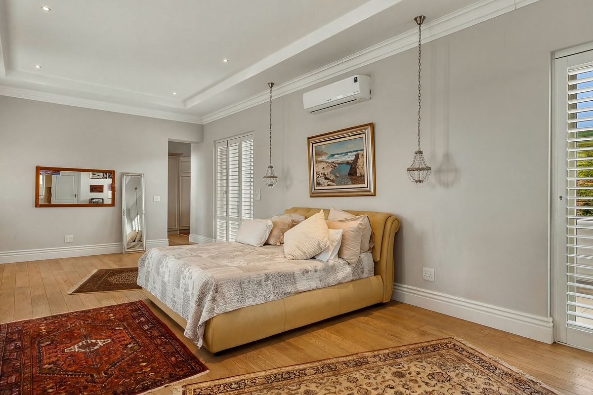 Spacious bedroom featuring timber flooring, crown molding, recessed lighting, and plantation shutters, complemented by a wall-mounted air conditioning unit.