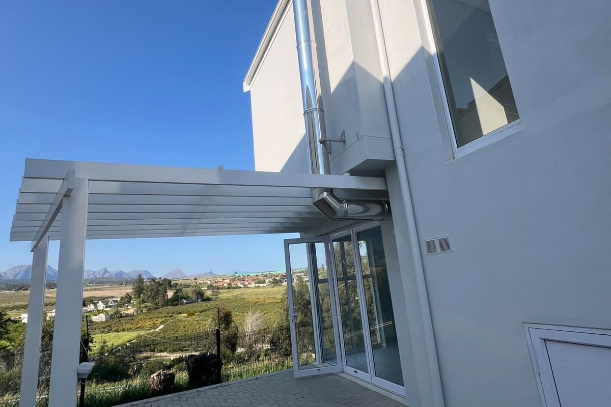 Rear exterior view of the townhouse featuring a paved patio, white pergola, and external fireplace flue with scenic landscape views.