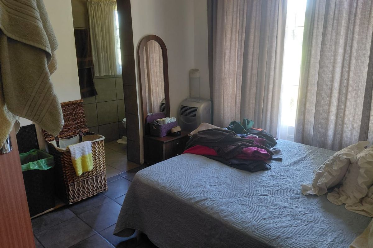 A bedroom featuring tiled flooring and direct access to an en-suite bathroom, with large windows dressed in curtains.