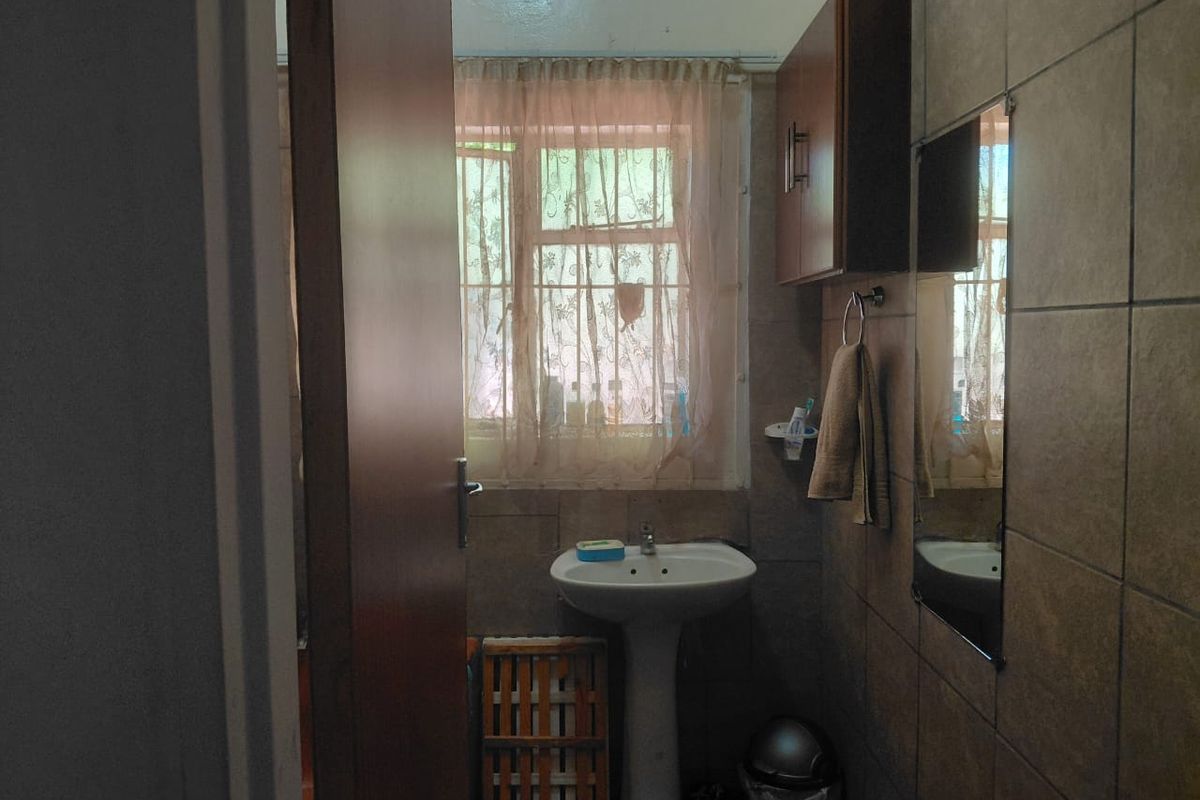 A compact bathroom featuring a pedestal basin, wall-mounted storage cabinet, and full-height wall tiling.