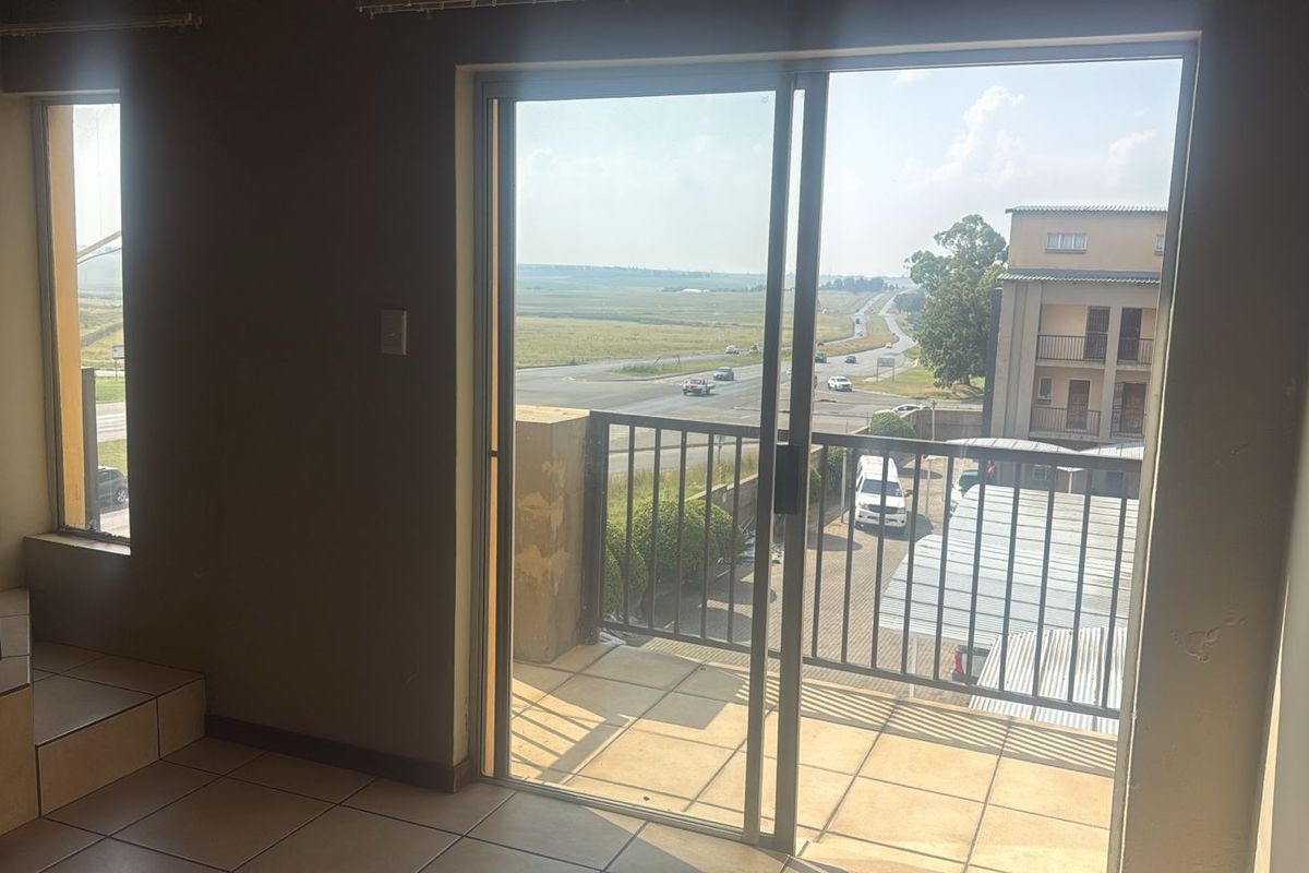 Interior view of a living area featuring tiled flooring and a sliding glass door leading to a balcony with an elevated road view.
