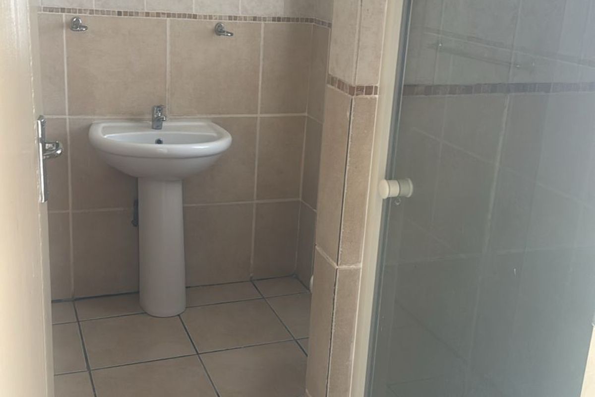 A functional bathroom featuring a pedestal basin, tiled walls and flooring, and a glass-enclosed shower stall.