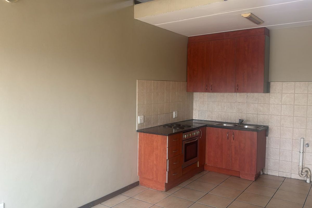 Compact kitchen featuring wooden cabinetry, built-in oven and hob, tiled splashback, and tiled flooring in an open-plan layout.