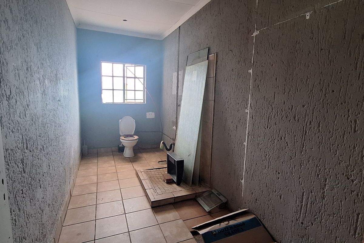 An unfinished bathroom space featuring tiled flooring, a toilet, and exposed wall surfaces, requiring completion and renovation to become a functional room.