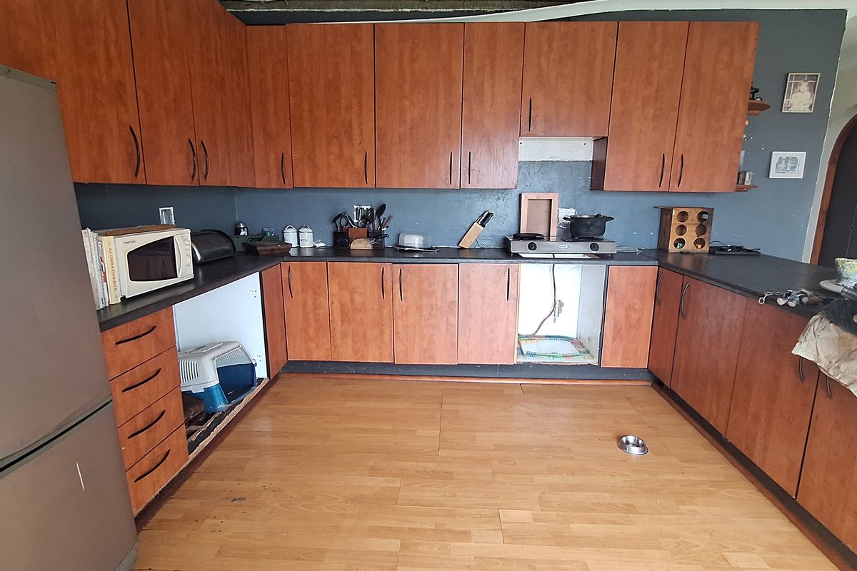 A dated kitchen featuring wood-look cabinetry, dark countertops, and laminate flooring, currently requiring repairs to the ceiling and cabinetry.