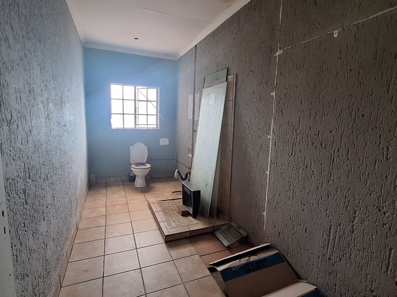 An unfinished bathroom space featuring tiled flooring, a toilet, and exposed wall surfaces, requiring completion and renovation to become a functional room.