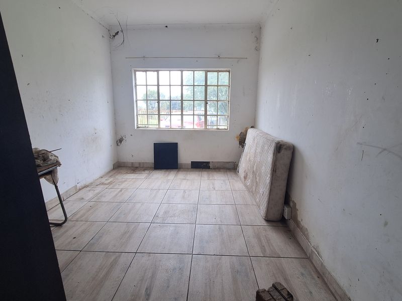 A vacant bedroom featuring tiled flooring and a large window, requiring cosmetic updates and wall repairs to restore its condition.