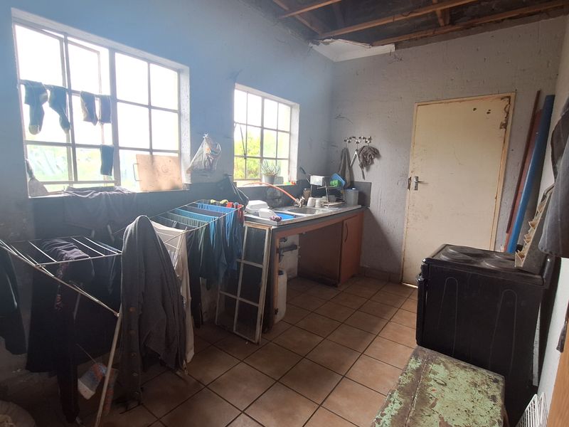 A utility space featuring a basic sink unit, tiled flooring, and exposed ceiling rafters, requiring significant renovation and finishing work.