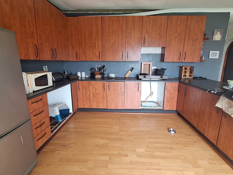 A dated kitchen featuring wood-look cabinetry, dark countertops, and laminate flooring, currently requiring repairs to the ceiling and cabinetry.