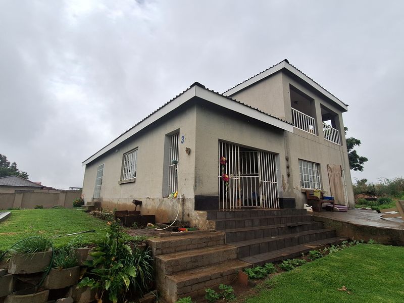 Two-story residential house featuring a tiled entrance staircase, security gates, and a surrounding lawn area with retaining wall landscaping.