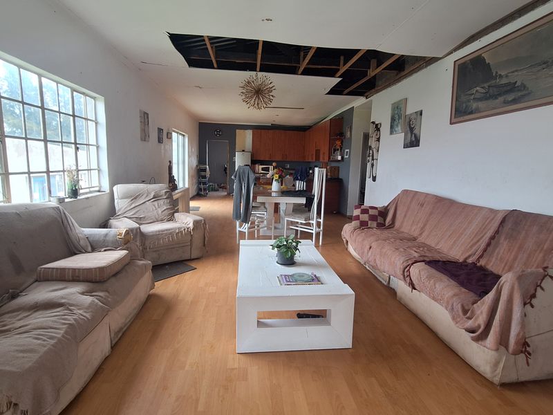 Open-plan living and dining area featuring wood-look flooring and large windows, currently requiring significant ceiling repairs.