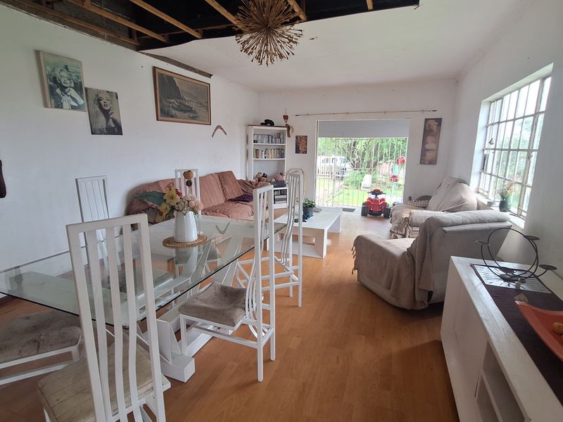 Open plan living and dining area featuring laminate flooring and large windows, currently requiring significant ceiling repairs and general maintenance.