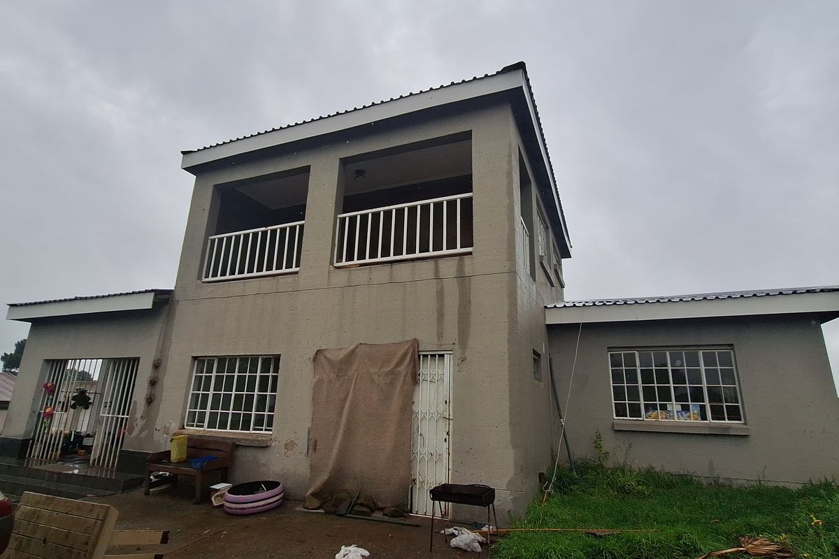 Two-story residential property featuring a balcony, metal security gates, and windows with burglar bars, set on a plot with a concrete patio area.