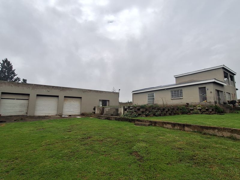 Exterior view of the property featuring a large lawn, a multi-car garage block, and the main dwelling with a retaining wall structure.