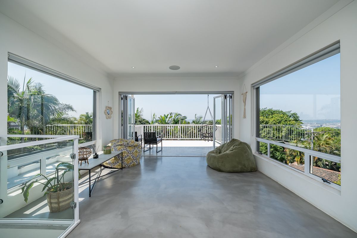 Bright living area featuring polished concrete floors, large windows, and bi-fold doors opening onto a spacious balcony with scenic views.