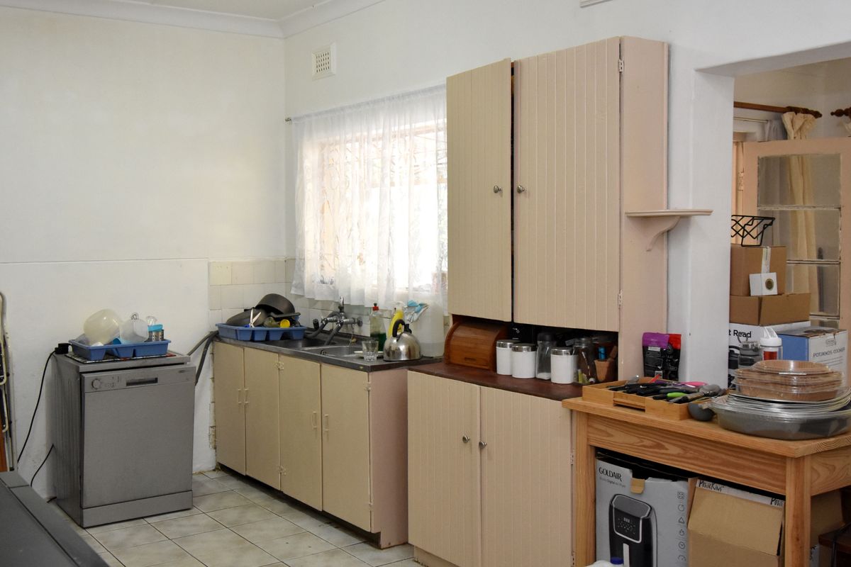 A dated kitchen featuring original cabinetry, a stainless steel sink, and tiled flooring, offering a functional space with potential for modernization.
