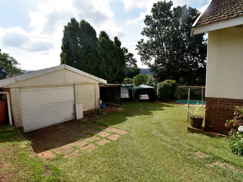 Rear garden view featuring a detached garage, lawn area, and a glimpse of the swimming pool, offering potential for outdoor landscaping and improvement.